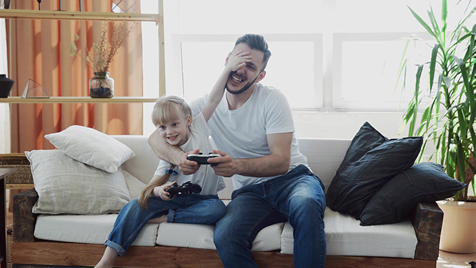 Father and daughter sitting on a couch playing video games