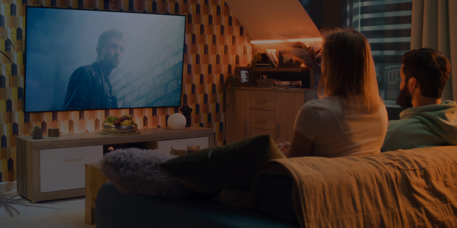 A man and woman sits on a couch streaming a movie while watching intensely.